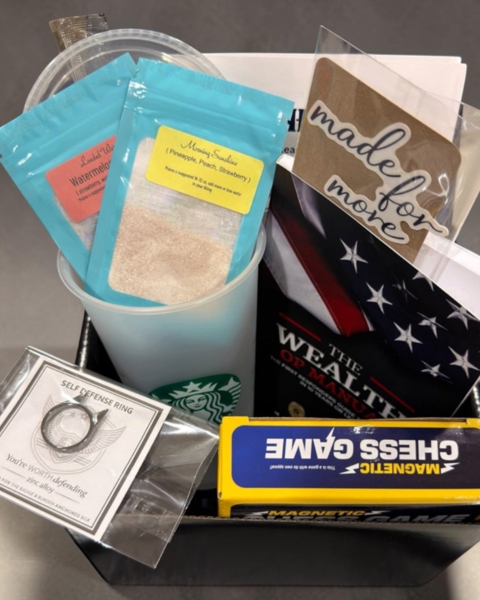 April Financial Readiness ANCHORED Box with The Wealth OP Manual, drink mixes, reusable cup, self-defense ring, magnetic chess game, and sticker