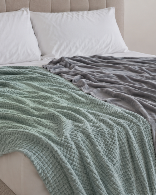 Two cooling blanket styles draped across a bed for hot sleepers and daytime sleep