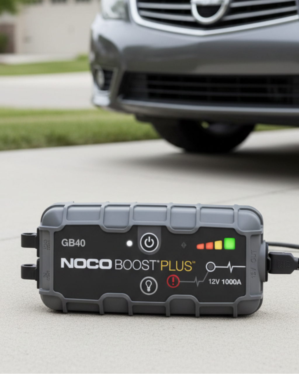 NOCO Boost Plus GB40 portable jump starter positioned beside a vehicle in a residential driveway