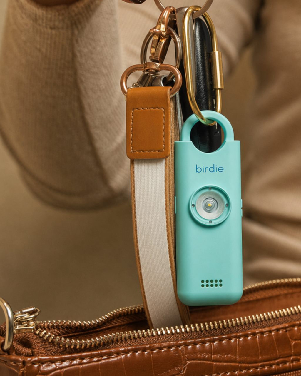 Aqua She’s Birdie personal safety alarm attached to a brown purse with a white-and-tan key strap